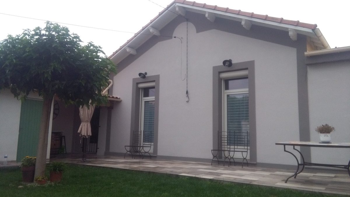 Façade de maison repeinte en gris clair avec des encadrements de fenêtres plus foncés.