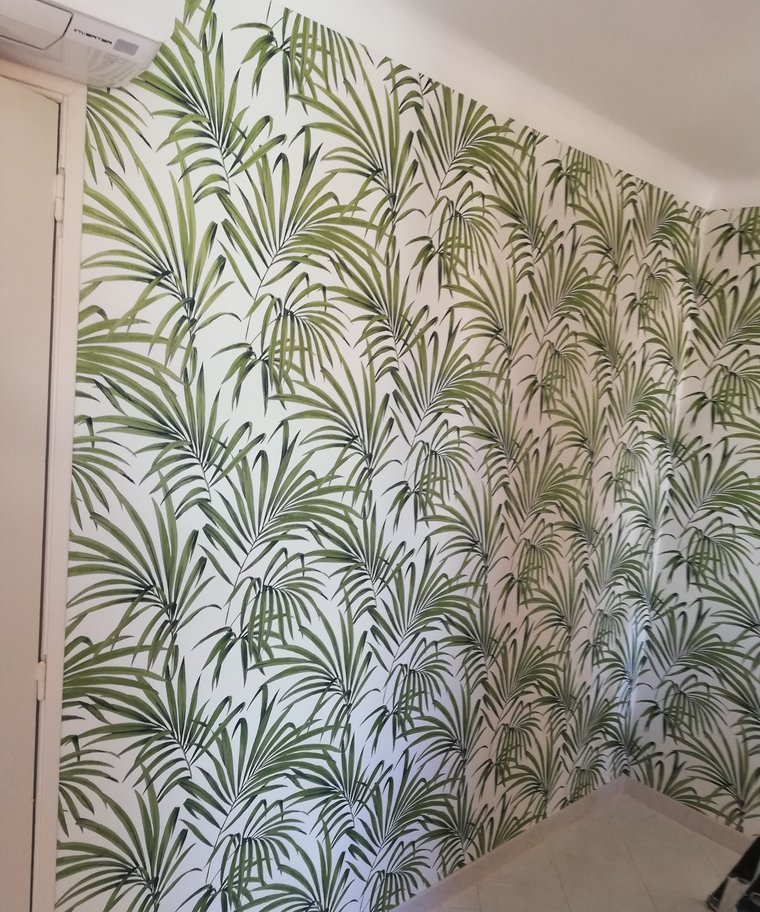 Mur d'angle tapissé d'un papier peint à motif de palmes vertes, raccord suivi dans l'angle.